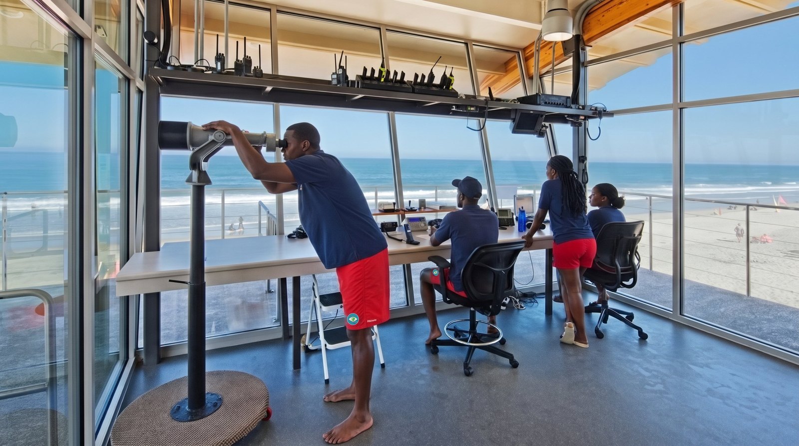 Intérieur du poste de surveillance du Mirador Tropicana : nageurs-sauveteurs de Sauvons la Planète, longue-vue sur pied, pupitre de coordination, radios et écran de suivi face à la zone de baignade